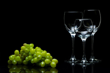 Glasses for wine and a bunch of grapes on a black background