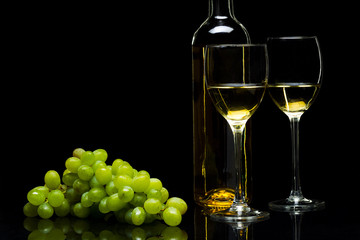 Glasses for wine and a bunch of grapes on a black background