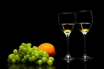 Glasses for wine, grapes and oranges on a black background