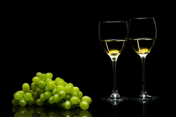 Glasses for wine and a bunch of grapes on a black background