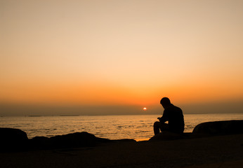Silhouette of young man, standing alone, lonly by the sunset light of sea