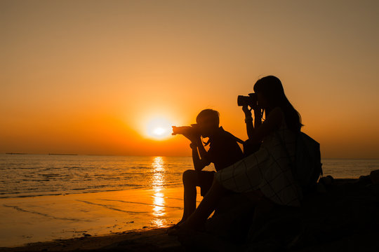 Silhouette of love, lover young man and woman photographer taking image On sunset the beach, romantic shot