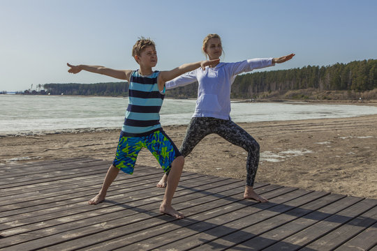 Young Woman And Boy Child Practicing Yoga, Mother And Son Standing In Warrior Position Exercise, Virabhadrasana Pose, Sea Beach