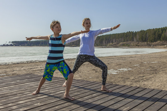 Young Woman And Boy Child Practicing Yoga, Mother And Son Standing In Warrior Position Exercise, Virabhadrasana Pose, Sea Beach