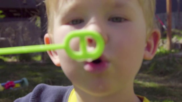 Adorable little boy leans in close to camera and blows bubbles toward the lens