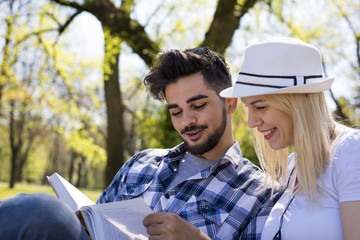 Young couple sitting on the park bench and reading book on beautiful sunny day