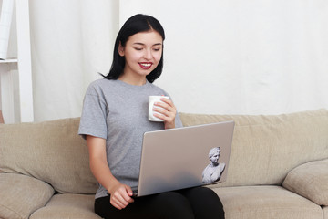 Pretty young woman working on a laptop while drinking cup of tea