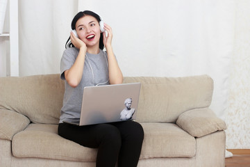 woman using laptop computer and headphones, sitting on living room