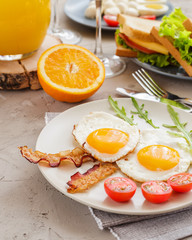 Breakfast table with fried eggs, bacon, cherry tomatoes, sanwiches