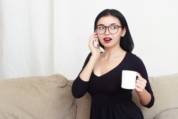 young happy beautiful woman on couch talking on mobile phone drinking cup of tea