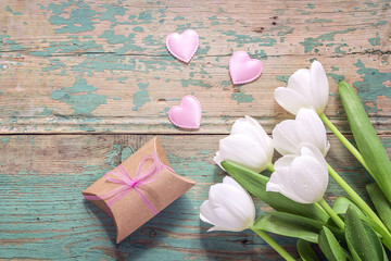 White tulips, hearts and gift box on a turquoise grunge wooden background. Top view with copy space.