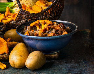 Cooked forest Mushrooms in rustic bowl and potato on dark rustic background, front view. Autumn cooking concept