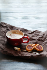 Cup with coffee and cherry shaped cookies with linen napkin on wooden background