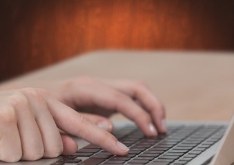 Hand typing on laptop with brown background