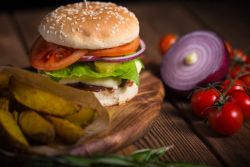 Large appetizing burger with beef, potatoes and cheese on a wooden surface. Close-up
