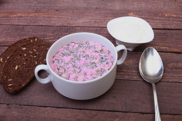 Popular spring cold soup okroshka with yoghurt. Okroshka in a bowl, sour cream and slices bread on wooden table. Selective focus