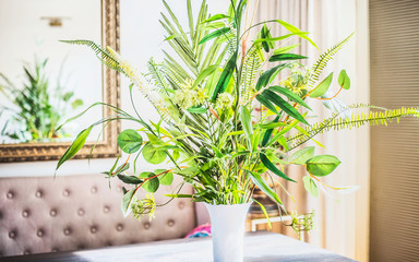 Beautiful green  bunch with various plants leaves in vase at room background. Home interior and decor