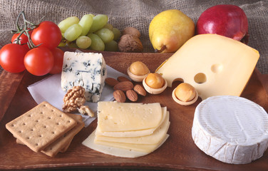 Assortment of cheese with fruits, grapes and nuts on a wooden serving tray.