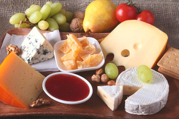 Assortment of cheese with fruits, grapes and nuts on a wooden serving tray.