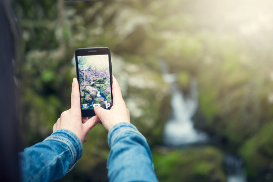 Young woman taking a photo with her phone of the falls in the middle of nature