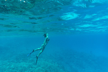 Naklejka premium Young lady swimming underwater over coral reefs in a tropical sea