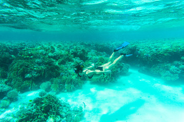 Underwater shot of the young lady gliding over vivid coral reef on a breath hold in sea water