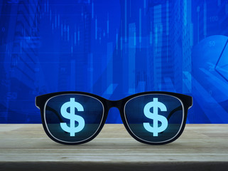Dollar currency icon with eye glasses on wooden table over financial graph and city tower background, Business success concept