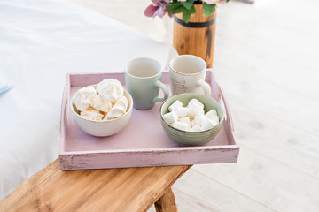 A pink breakfast tray on which lie cups for tea and for coffee, white marshmallows are in the plates