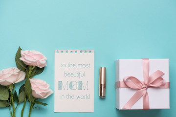Mother's Day concept. Bouquet of pink roses with gift box and lipstick. Blank paper note for copy space.