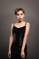 Fototapeta premium Sexy attractive asian woman posing in fashionable black dress over grey background