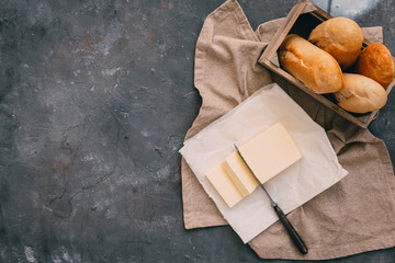 Pat of fresh farm butter  with a knife and bread over rustic background - obrazy, fototapety, plakaty