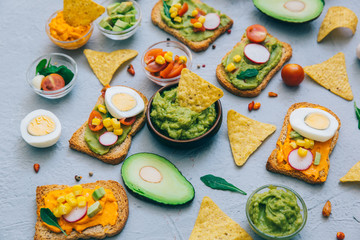 Guacamole and toasts. Fresh ingredients - avocado, tomatoes, onio, garlic, cilantro and crackers on gray background. Top view