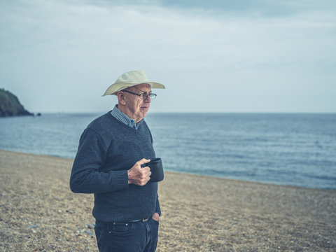 Senior man on beach with cup of drink