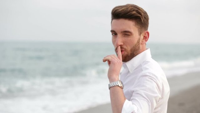 Ragazzo con camicia bianca fa il simbolo del silenzio con il dito indice sul naso. Zittisce in camera. 