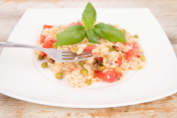 Risotto with tomato and pea on a wooden background being eaten with a fork