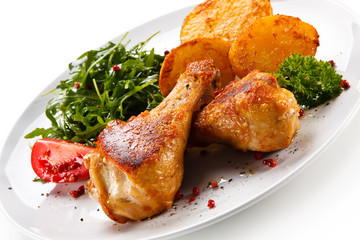 Roast chicken drumsticks with potatoes on white background
