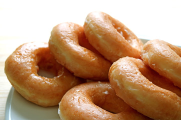 Piled up sugar-glazed doughnuts served on white plate, closed up, white background 