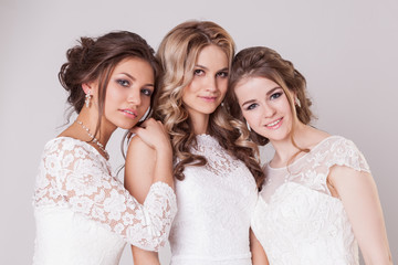 Wedding make-up, hairstyle and dresses. Three brides pose in studio on grey background
