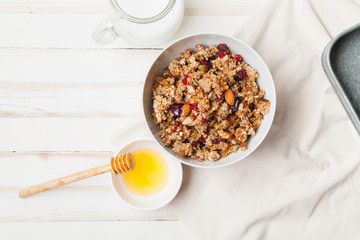 Morning granola with dried fruits, honey, milk and berries on white wooden background. Top view...