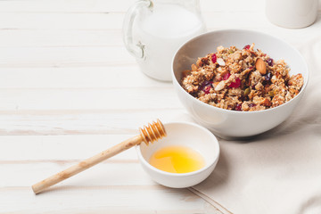 Morning granola with dried fruits, honey, milk and berries on white wooden background. Side view iwth copy space