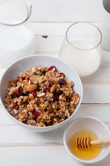 Morning granola with dried fruits, honey, milk and berries on white wooden background. Top view with copy space