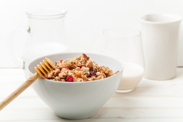 Morning granola with dried fruits, honey, milk and berries on white wooden background. Side view with copy space