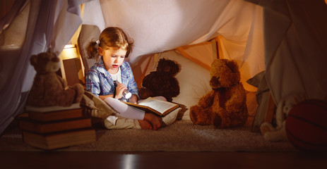 Obraz na płótnie Canvas child girl with a book and a flashlight and teddy bear before going to bed.