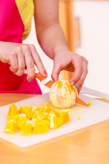 Woman housewife in kitchen cutting orange fruits
