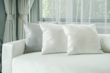 Pillows lay on white sofa with sheer curtain in background - obrazy, fototapety, plakaty