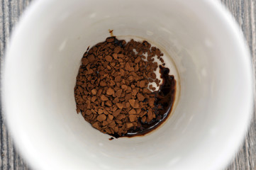 Mug of hot instant coffee on a wooden table with a spoon
