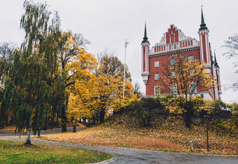 Obraz premium Admiralty House, golden trees and fallen leaves on Skeppsholmen islet in Stockholm by autumn cloudy day. Amiralitetshuset building near Skeppsholm bridge.
