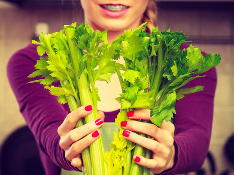 Woman in kitchen holds green celery