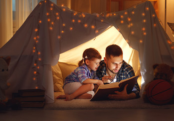 happy family father and child daughter reading a book  in  tent at home.