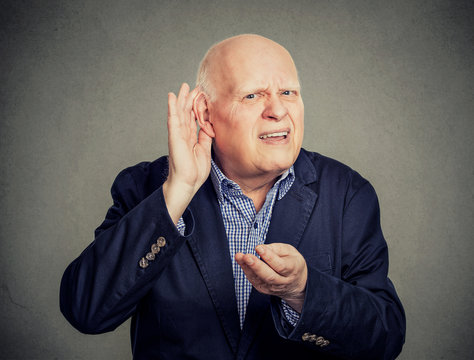 Senior man, hard of hearing, placing hand on ear asking someone to speak up